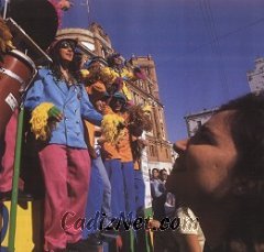 Cadiz:Los coros ofrecen sus coplas desde la batea de sus carrozas, la plaza del Mercado es un hervidero de sones con raíces caribeñas de ritmo contagioso. En la foto vemos al coro Trinidad, que destacaba especialmente por su tipo colorista. Al fondo, el edificio de correos. Al usar un gran angular situamos al sujeto en relación con su entorno creando un mayor dinamismo y dando mayor información en la toma.